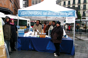 Delante del stand de Plaza Callao, Itxaso, (d) y  Trini (c), colaboradoras responsables del área hispana de Universelles Leben (Vida Universal) en Alemania, junto a uno de  los colaboradores españoles de la organización.