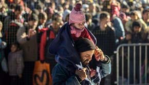 Un refugiado carga con su hijo al cruzar la frontera entre Eslovenia y Austria 