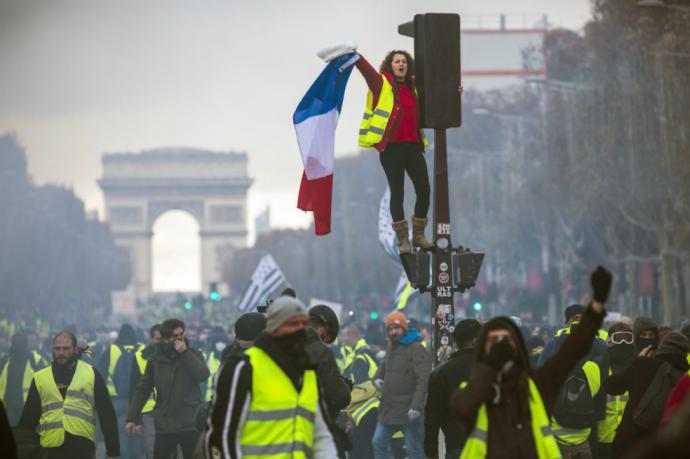 Una mujer, parte de los "chalecos amarillos" grita consignas subida a un semáforo durante una protesta en los Campos Elíseos en París, Francia.