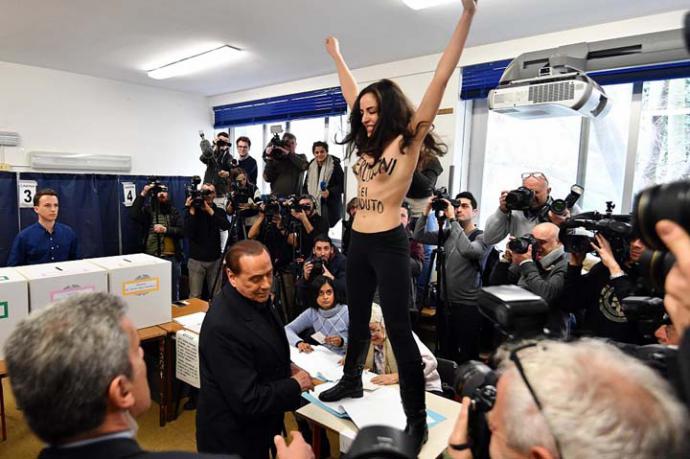 Una protestante del grupo Femen sorprende al exprimer ministro Silvio Berlusconi durante la jornada de votación en Milán, Italia.