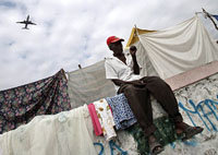 El avión de American Airlines, recortado en el ciel al aproximarse al aeropuerto. En primer plano un damnificado haitiano en su improvisada vivienda